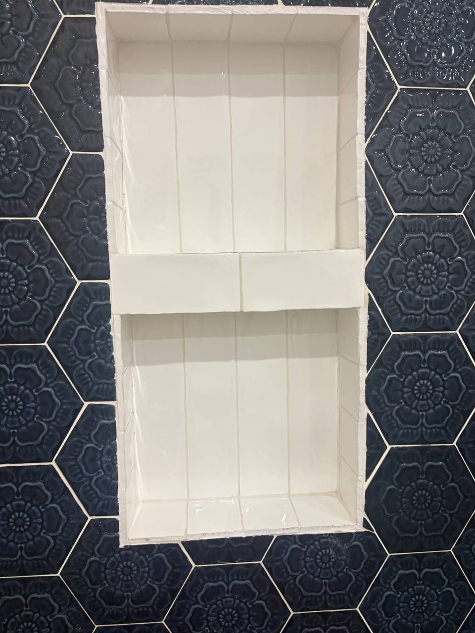 Built-in shower niche with dark blue hexagonal floral tiles and white shelving
