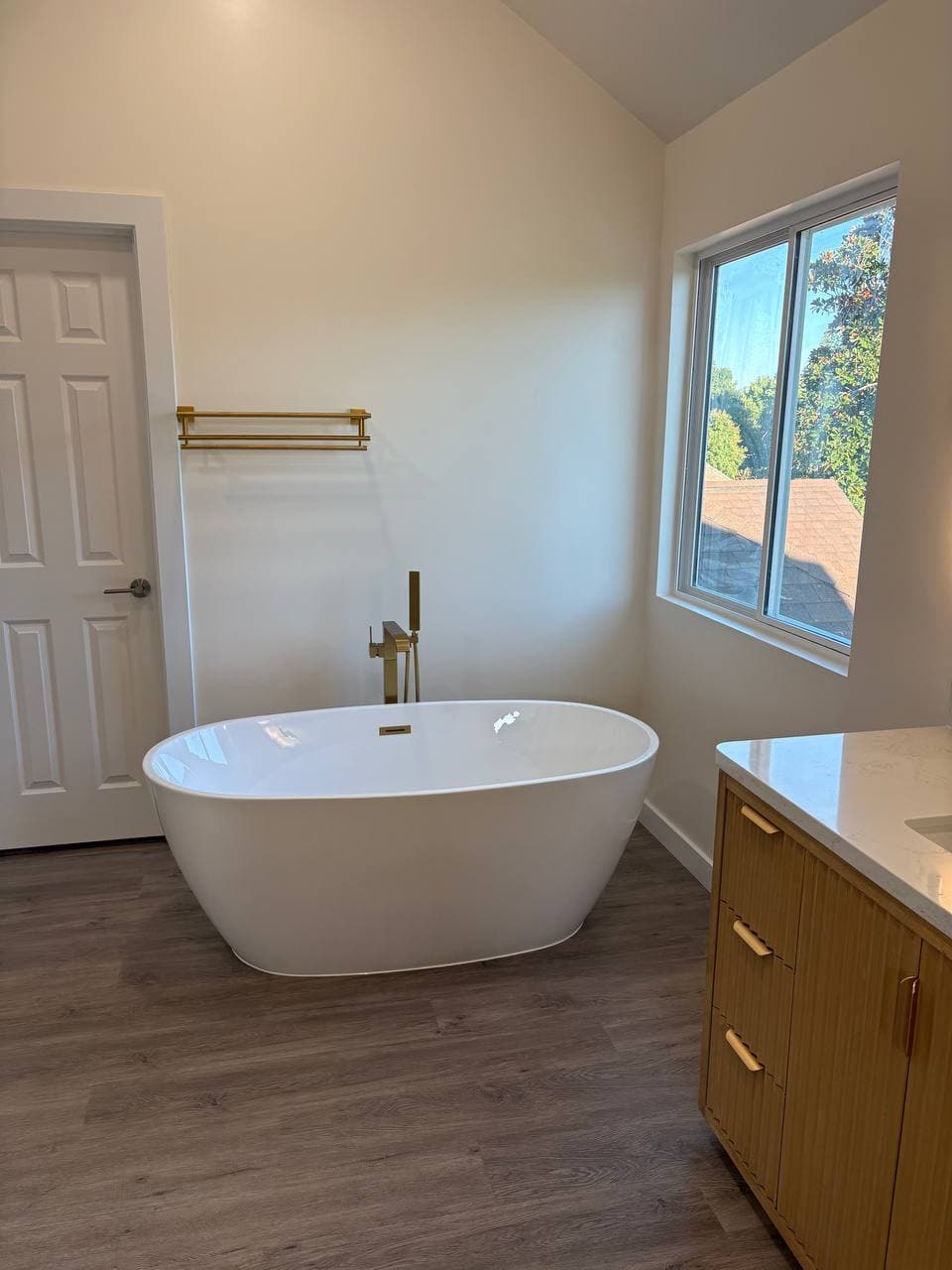 Freestanding white soaking tub with gold floor-mount faucet and towel rack