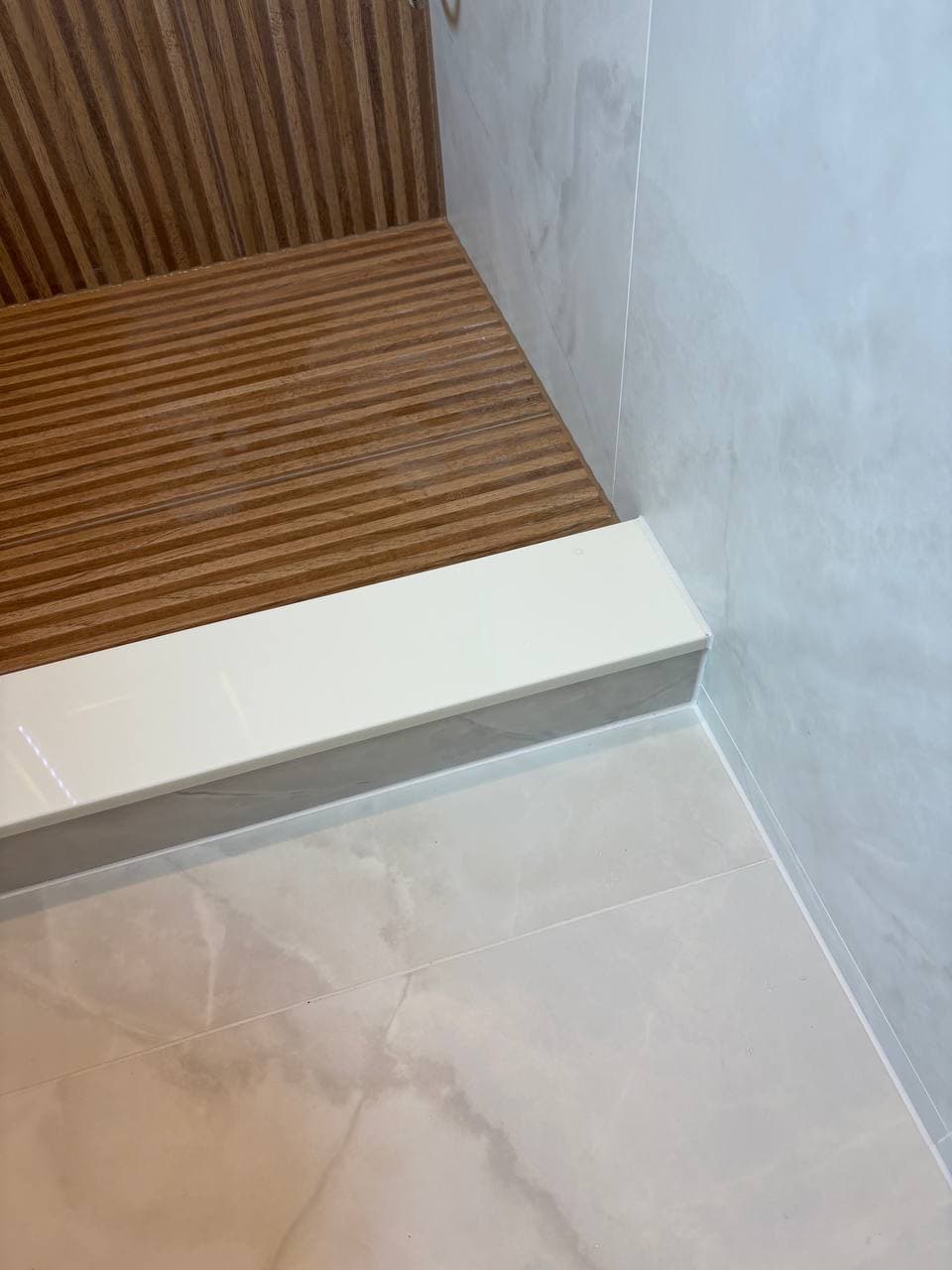 Teak shower floor detail meeting clean white marble curb