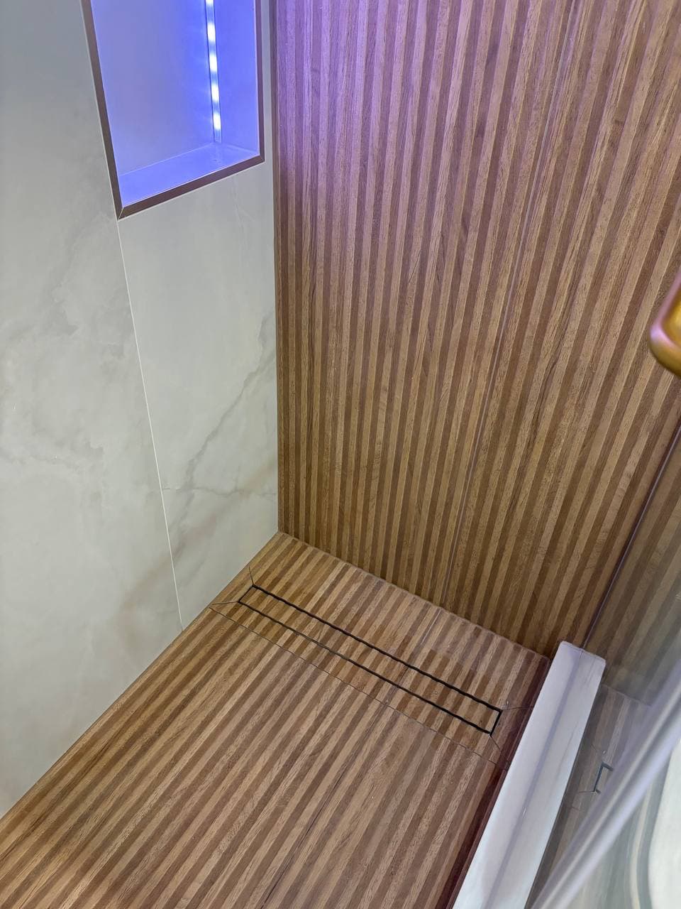 Wood-paneled shower floor with linear drain and LED accent niche